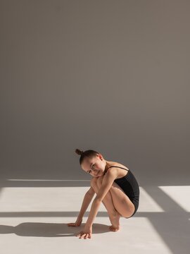 Little Caucasian girl gymnast in a black leotard posing on a white background. 