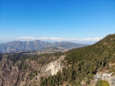 "Panoramic Himalayan view from Gangolihat hill top in Pithoragarh, Kumaon region of Uttarakhand, showcasing distant snow capped peaks of Nanda Devi, Panchachuli, and Nanda Ghunti under a clear bluesky