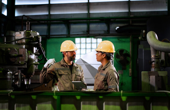 Two industrial technicians inspect metal component precision and discuss quality control in factory