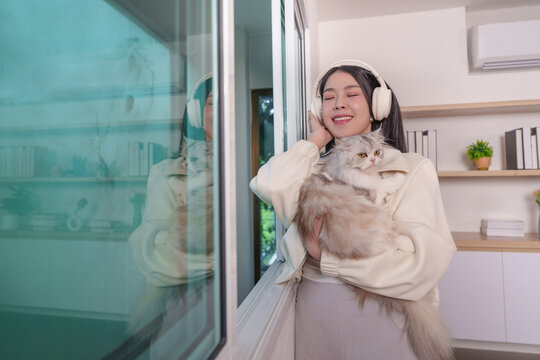 Asian woman listening to music with headphones while holding cat at home