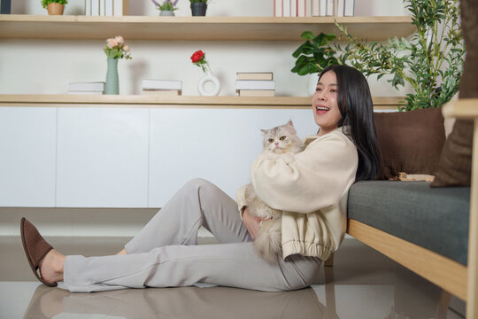 Asian woman sitting on floor hugging pet cat in modern living room