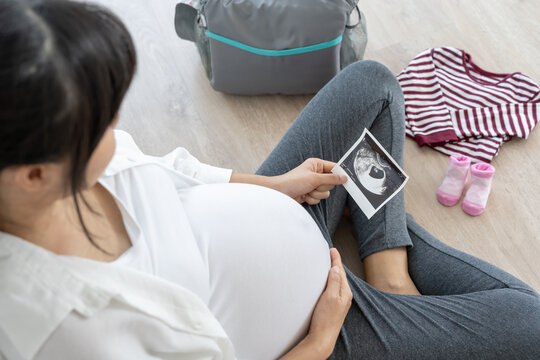 pregnant woman is looking at an ultrasound photo of fetus. Mother gently touches the baby on stomach. Happy, family, growth, pregnancy, enjoyment , prepare newborn, take care, healthcare, tummy.