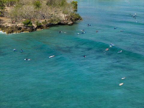Aerial view of surfers on surfboards in the turquoise waters of Nusa Dua Beach with rocky coastline in Kecamatan Kuta Selatan, Bali, Indonesia.