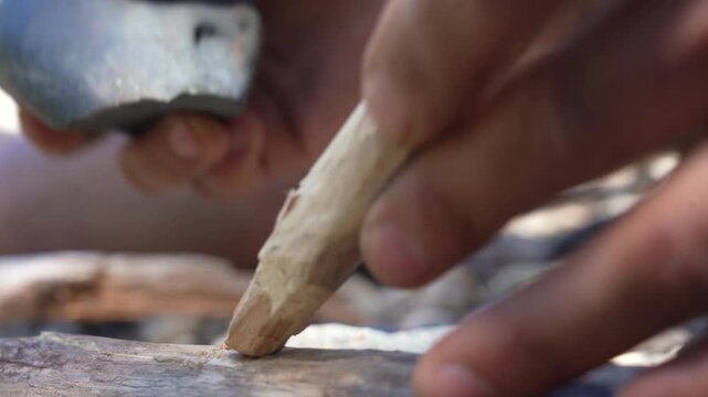 Close up of primitive flintknapped stone blade being used to carve and cut wooden stick outdoors