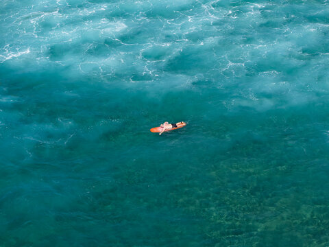 Aerial view of a surfer paddling on a surfboard in the clear turquoise waters of Nusa Dua Beach, Kecamatan Kuta Selatan, Bali, Indonesia.