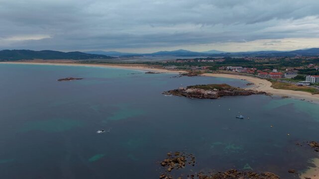 Aerial - Long sandy A Lanzada beaches with rocky islet and chapel headland near Sanxenxo Spain
