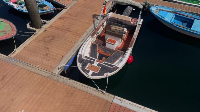 Wooden decked motor boat moored at a pontoon berth beside blue boats in a sunlit marina