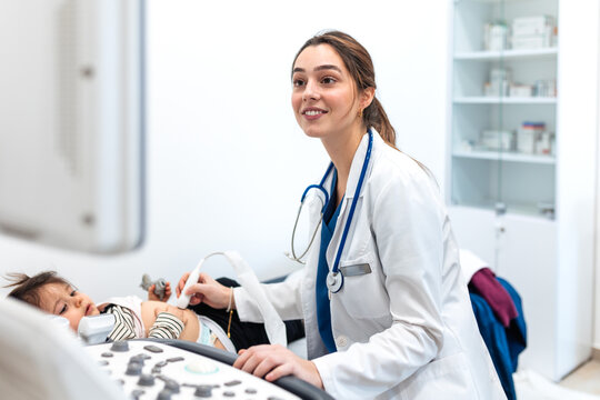 Female doctor performing an ultrasound examination on a young child lying on an examination table in a modern medical clinic. Healthcare and pediatrics concept.