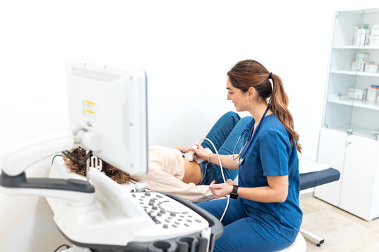 Female doctor performing an abdominal ultrasound examination on a female patient lying on an exam table in a modern clinic. Healthcare and diagnostics medical technology concept.