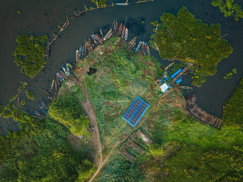 Aerial view of Lake Rawa Pening featuring a peninsula with wooden boats moored along the shore, lush green vegetation, and a structure with solar panels in Waduk Rawapening, Central Java, Indonesia.