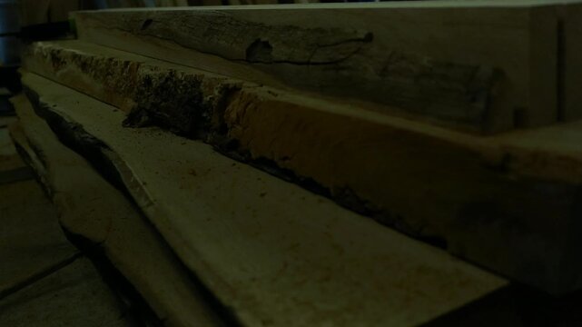 Close up view of stacked raw oak lumber with natural edges, showing the beautiful texture and grain of the unprocessed wood piled in a carpenter's workshop for woodworking projects