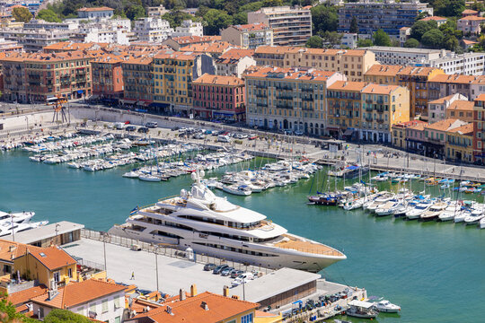 Aerial view of the Port of Nice with a large luxury yacht docked at the pier, surrounded by colorful historic buildings and sailboats in Nice, Provence-Alpes-Cote d'Azur, France.