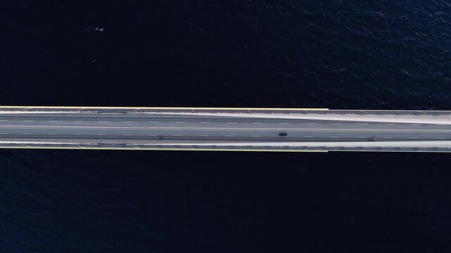Top-down drone shot of Rio-Antirrio Bridge at sunset. Towering pylons and vehicles visible from above. Golden evening light.