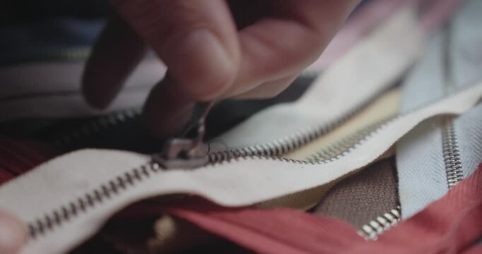 Close-up of a tailor checking coloured clothing zips on a worktable, highlighting garment construction, sewing preparation and fashion production.