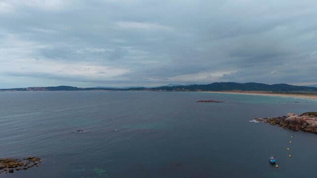 Aerial - A Lanzada Beach bay with small boat and rocky islets on the Galicia coast Spain