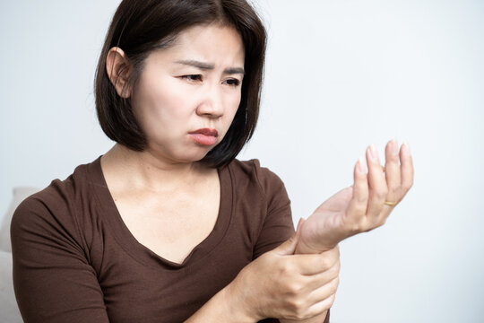 Asian woman holding her wrist in severe pain, suffering from carpal tunnel syndrome, arthritis, joint inflammation, or office syndrome injury