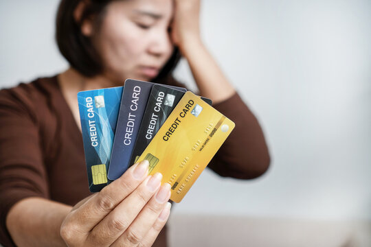 Stressed Asian woman holding multiple credit cards with headache, suffering from debt burden, financial crisis, bankruptcy, and overspending problems