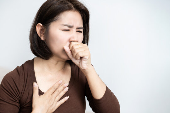 Asian woman coughing into fist with chest pain, suffering from flu, cold, bronchitis, coronavirus infection, or throat irritation