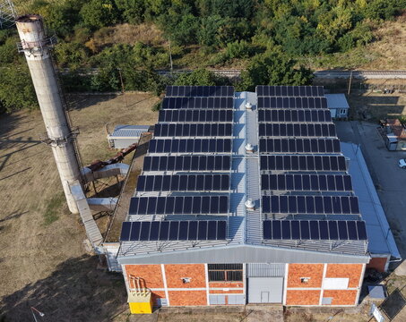 Aerial view of an industrial building in the south industrial zone featuring a large array of solar panels on its roof and a tall chimney, surrounded by trees in Pancevo, Serbia.