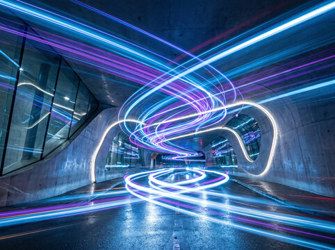 Abstract Blue and Purple Neon Light Trails Swirling Through a Futuristic Concrete Tunnel Representing High-Speed Data Transmission and Cyber Connectivity