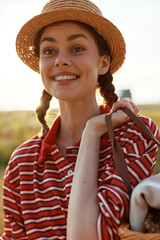 Obraz premium Young woman with braided hair wearing a straw hat and striped shirt outdoor. Lifestyle portrait happy female enjoying nature sunny day concept for summer recreation.