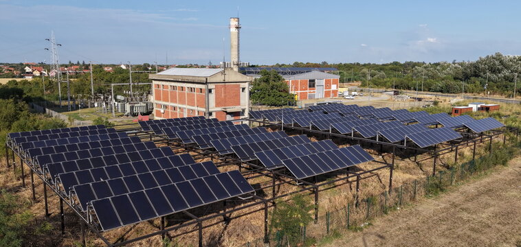 Aerial view of solar panels in the south industrial zone with a brick building and a tall chimney in the background in Pancevo, Serbia.