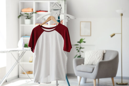 White and maroon raglan t-shirt on a clothes steamer in a bright laundry room with an ironing board and shelving