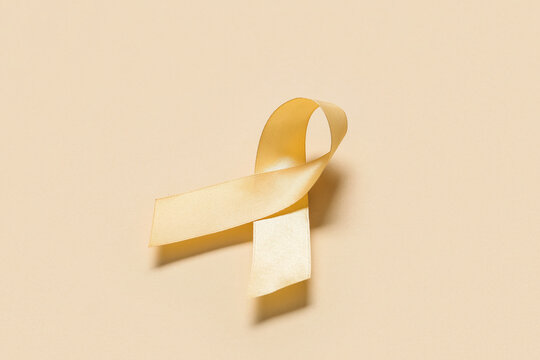 Golden awareness ribbon on a light beige background, childhood cancer support and various health causes