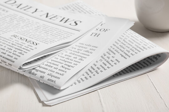 Folded daily newspaper with business section and lorem ipsum text on a white wooden table, news and information