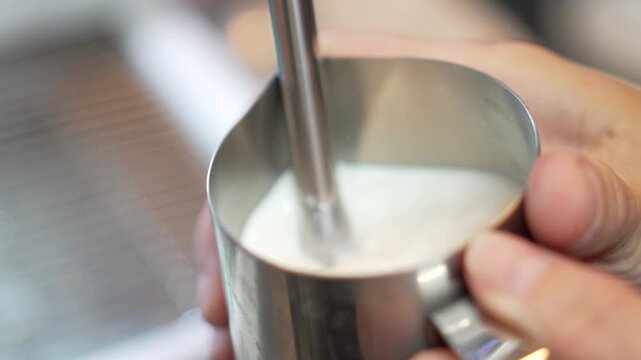 Steaming milk pitcher barista prepares frothed milk in a stainless steel jug for a latte in a cafe