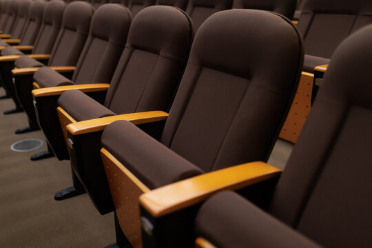 Empty Rows Of Comfortable Modern Armchairs Inside Cinema Theater Auditorium. Row of classic dark fabric seats with wooden armrests in empty hall