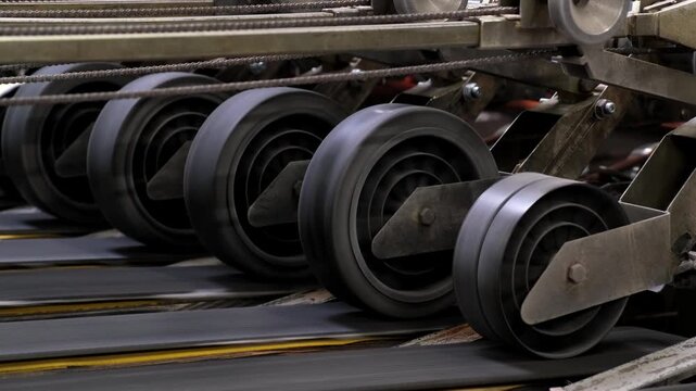 Detailed view of multiple rotating rubber rollers driving a transport belt mechanism inside an automated production plant.