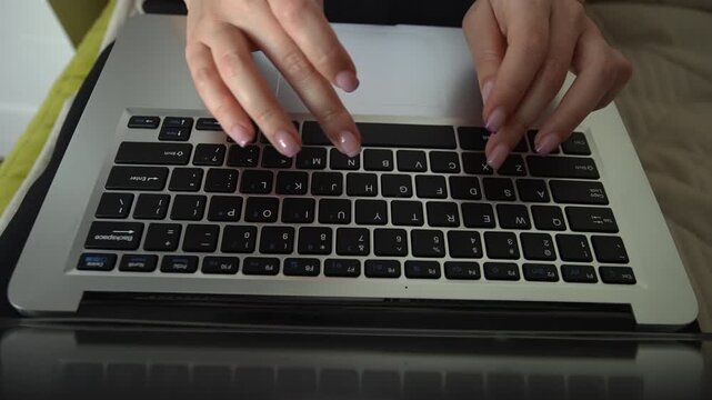 Top view of female fingers with beautiful manicure typing on laptop computer keyboard. Professional businesswoman working on project, sending email, chatting online from home office, close-up, slowmo.