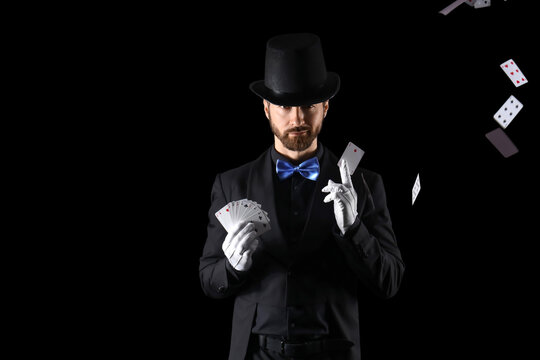 Male magician with playing cards on black background