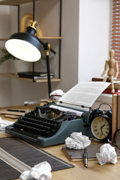 Vintage typewriter with crumpled paper and lamp on table in room