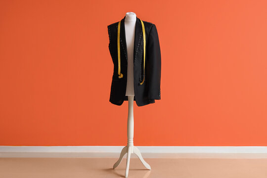Mannequin for tailor with half-finished jacket and measuring tape near orange wall