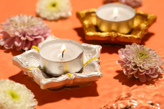 Diya lamps with burning candles and beautiful flowers in water on orange background. Divaly celebration