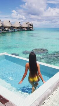 Luxury resort travel vacation destination idyllic overwater bungalow villa woman by pool. Social media influencer luxurious lifestyle. Raw unedited vertical video of real woman model without makeup