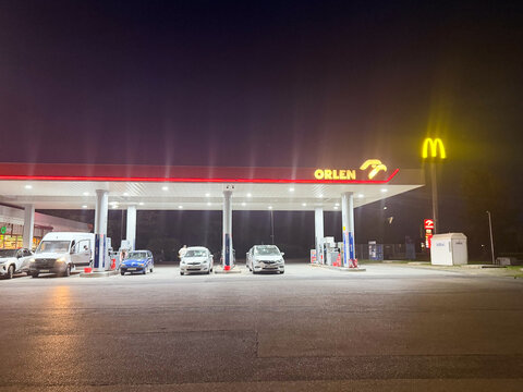 Illuminated gas station with parked cars and fast food signs at night