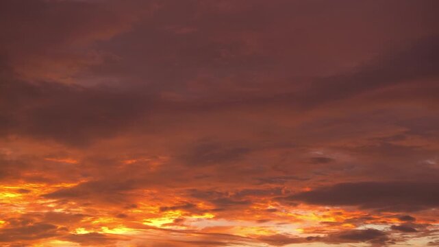 A sunset sky timelapse video capturing dense stratocumulus and altocumulus clouds glowing fiery orange and gold, with dramatic dark cloud layers creating a vibrant and intense evening atmosphere. 4k.
