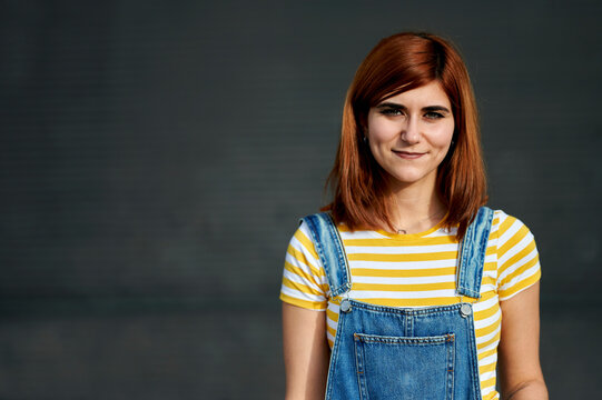 Young redhead woman smiling wearing denim overalls