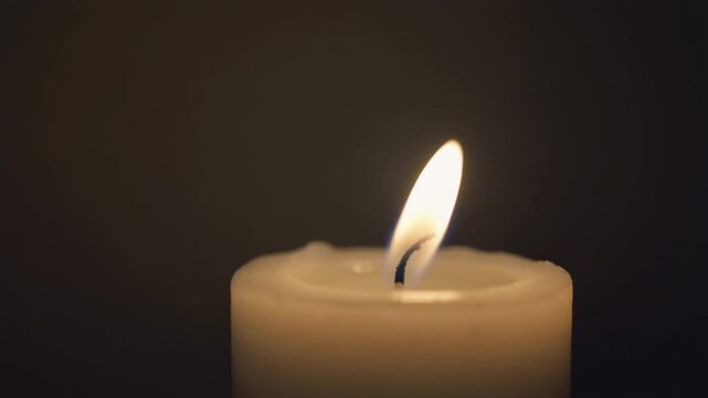White candle flame flickering softly on a dark warm background