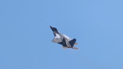 Obraz premium F-22 Raptor Fighter Jet Performing High-Speed Maneuver in Blue Sky