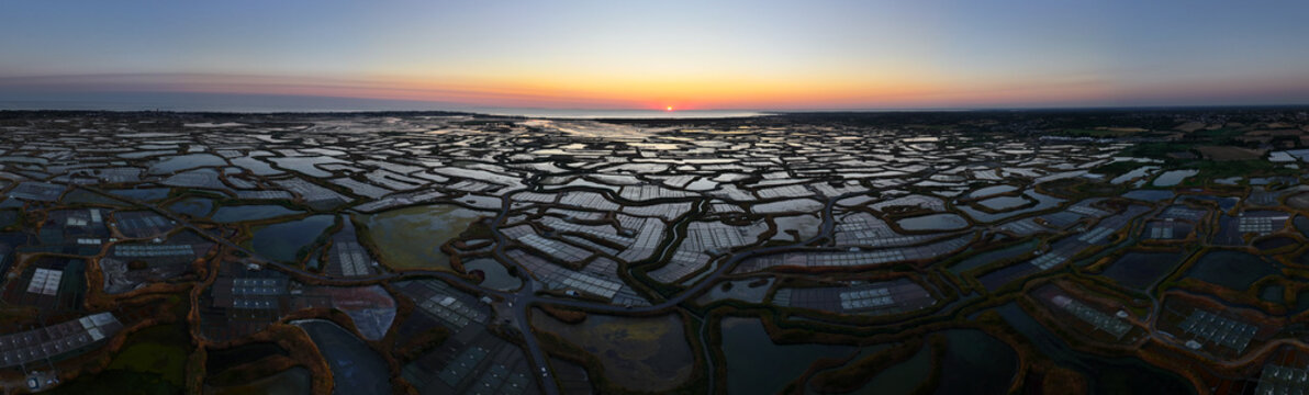 Aerial view of Marais salants de Guerande at sunset with reflective salt pools and golden light in Guerande, Pays de la Loire, France.