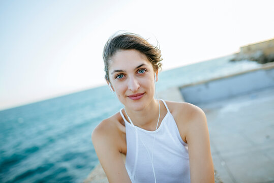 Portrait of young woman looking at camera with headphones with sea background.