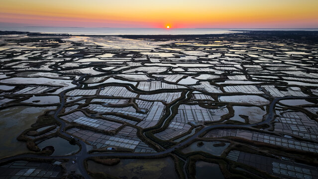 Aerial view of the Marais salants de Guerande salt pans at sunset, with reflective water pools and winding paths in Guerande, Pays de la Loire, France.