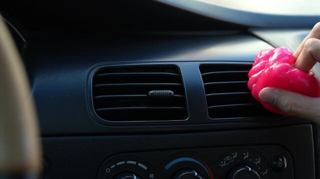 Man using pink cleaning gel to detail car interior. Close-up of hands pressing sticky slime into air vent to remove dust and dirt. Auto care and maintenance concept. Shooting in slow motion.