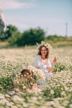 Young woman wearing Matricaria chamomilla wreath relaxes in sunny field with picnic basket during leisure time