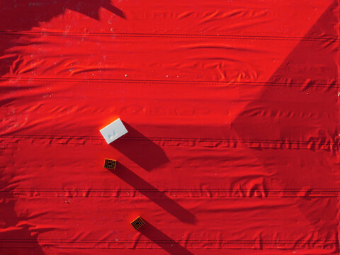 Aerial view of a vivid red tarp covering a roof, with small objects casting long geometric shadows in Belgrade, Serbia.
