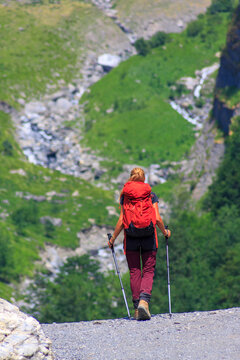 Woman hiking in mountains with backpack and trekking poles back view active outdoor adventure